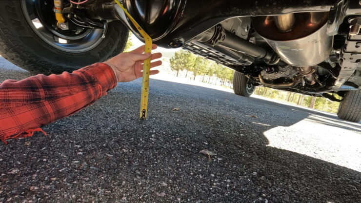 The man is measuring the ground clearance of his Toyota Tacoma